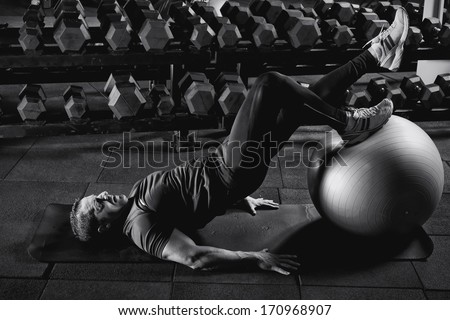 Man At The Gym Doing Exercises For His Abs With A Swiss Ball.Low Light. B&Amp;W Photo.