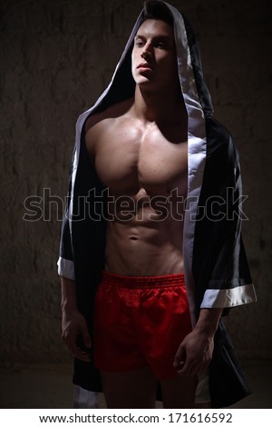 portrait of a young caucasian male fighter wearing a hooded sweater and patterned silk trousers.Low light.