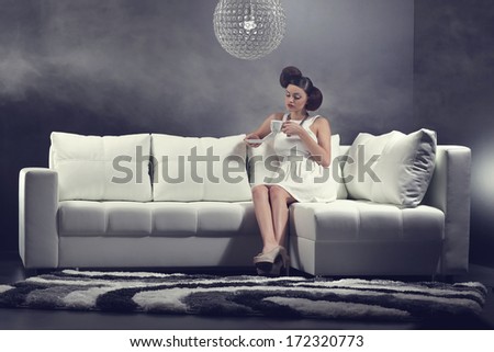 Beautiful elegant woman sitting on sofa and drinking coffee .Fashion colors