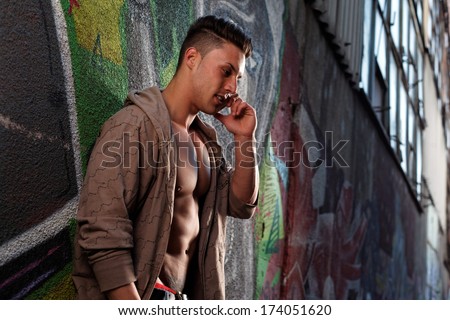 Sensual portrait of a very handsome muscular man with open shirt and hot body against window  on the phone in a ruins