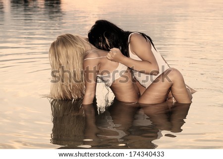 two women in a very erotic posing in the warm water at sunset .Fashion colors