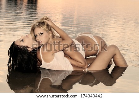 two women in a very erotic posing in the warm water at sunset .Fashion colors