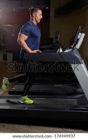 Concentrated athletic man training on a running machine in a fitness center .Low light