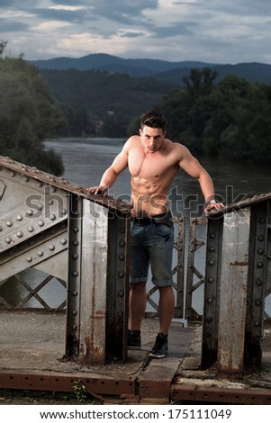 Handsome young muscle man shirtless with hand on rusty metal structure.Fashion colors.