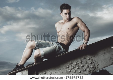 Handsome young muscle man shirtless with hand on rusty metal structure, looking in camera .Fashion photo