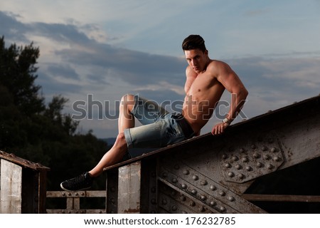 Handsome young muscle man shirtless with hand on rusty metal structure..Fashion photo