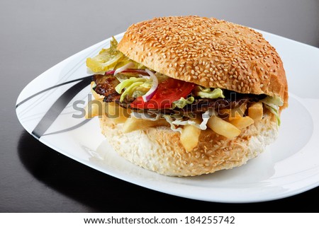 Delicious cheeseburger stacked high with a juicy beef patty, cheese, fresh lettuce, onion and tomato on a fresh bun with sesame seed standing on brown paper on a wooden tabletop with copyspace