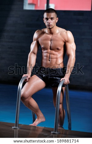 Stylized portrait of a young wet sexy muscular man standing in swimming pool .Shallow depth of field with focus on abdominals.