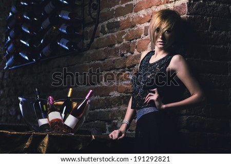 Attractive blonde woman  in elegant black dress sitting on bar stool. Gorgeous blonde model  posing provocatively in vintage bar