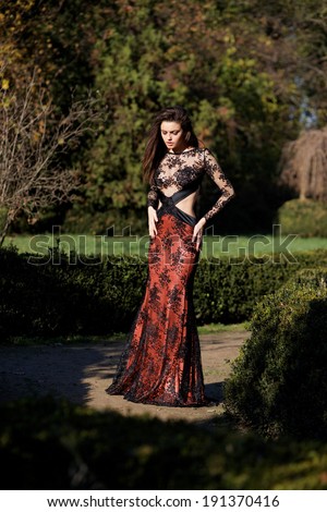 Beautiful slim girl in luxury dress in park on sunset. Romantic girl with glossy hair. Focus on a dress.