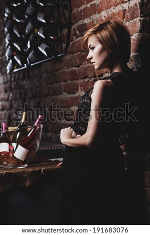 Attractive blonde woman in elegant black dress sitting on bar stool. Gorgeous blonde model posing provocatively in vintage bar