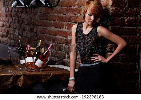 Attractive blonde woman in elegant black dress sitting on bar stool. Gorgeous blonde model posing provocatively in vintage bar