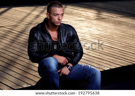 Attractive young muscle male model posing outdoors in black shirt and  leather jacket  .Fashion colors