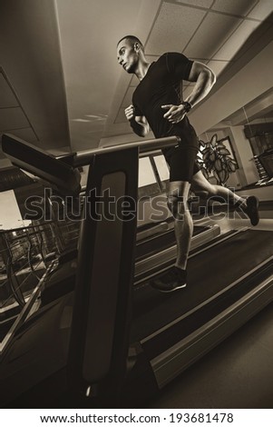 Muscle man running on treadmill .Wide angle.