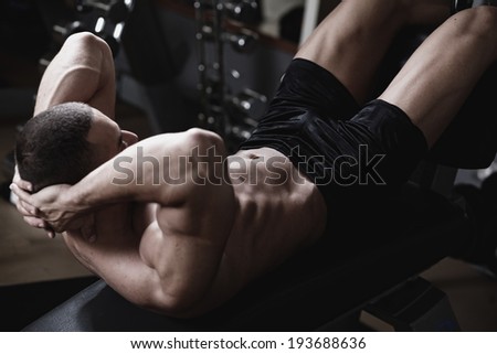 Bodybuilder man at abdominal crunch muscles exercises during training in fitness gym .Low light.