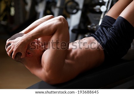 Bodybuilder man at abdominal crunch muscles exercises during training in fitness gym .Low light.