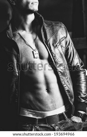 Attractive young muscle male model posing outdoors in black leather jacket and sunglasses .Fashion colors. Close up.
