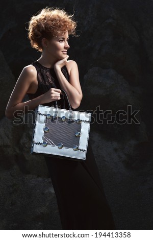 Fashion shot of a beautiful, professional model with a bag in her hands.Blonde beauty with bag posing outdoor.Fashion colors.