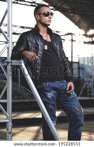 Attractive young muscle male model posing outdoors in black leather jacket and sunglasses .Fashion colors