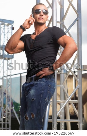 Attractive young muscle male model posing outdoors in black shirt and sunglasses .Fashion colors
