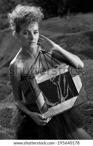 Fashion shot of a beautiful, professional model with a bag in her hands.Blonde beauty with bag posing outdoor.B&W.