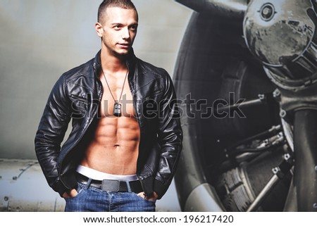 Attractive young muscle male model posing outdoors in black leather jacket .Fashion colors