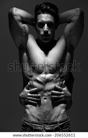 The very muscular handsome sexy guy on grey background, naked torso, black-and-white.Low light.