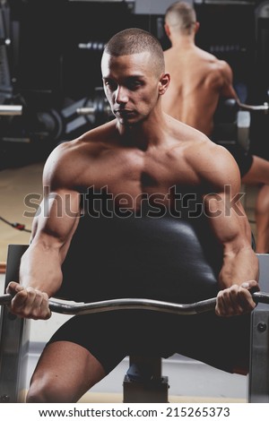 Closeup of a muscular young man lifting weights on dark background
