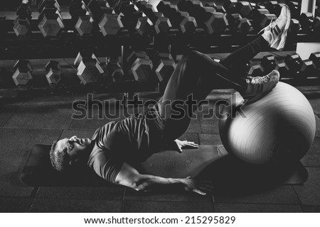Man at the gym doing exercises for his abs with a Swiss ball.Low light.