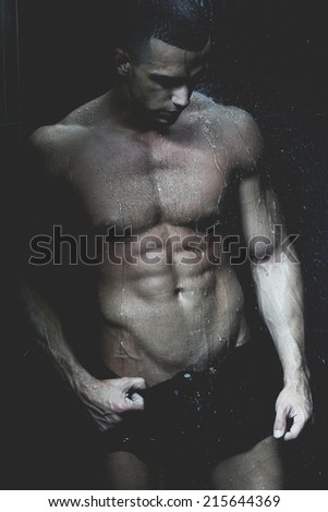 Strong man in chains posing under the rain, aqua studio .Low light .Shallow depth of field with focus on abdominals.