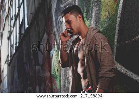 Sensual portrait of a very handsome muscular man with open shirt and hot body against window on the phone in a ruins