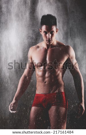 Strong man in chains posing under the rain, aqua studio .Glamour colors.