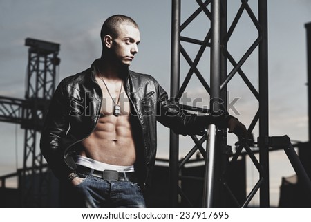 Attractive young muscle male model posing outdoors in leather jacket.Fashion colors