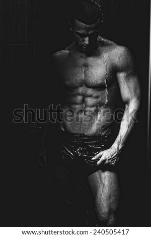 Strong man in chains posing under the rain, aqua studio .Low light .Shallow depth of field with focus on abdominals.