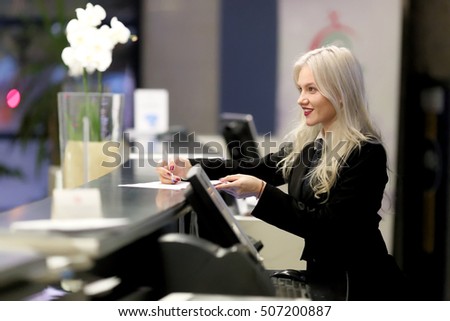 Hotel receptionist. Modern luxury hotel reception counter desk with bell. Happy female receptionist worker standing at hotel counter.