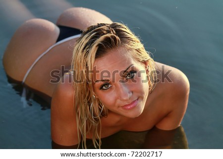 A blonde bikini model posing outdoors against a body of water