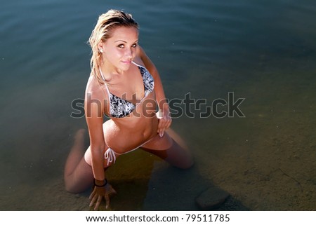 The beautiful bikini model posing against a setting sun on a body of water .Fashion art photo