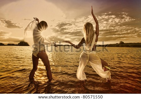 Two sexy girl posing against a setting sun on a body of water.Erotic art photo.