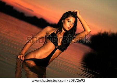 Beautiful brunette woman posing at sunset in the warm water of a lake
