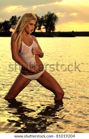 Beautiful blonde woman posing in the warm water at sunset