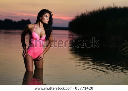 The beautiful bikini model posing against a setting sun on a body of water .Erotic art photo