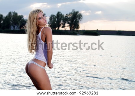 A blonde bikini model posing against a setting sun on a body of water