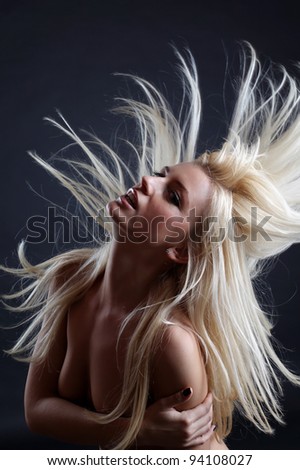 A beautiful blonde girl posing in a studio while playing with her crazy hair.