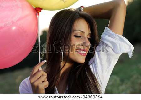 Happy brunette girl with balloons relaxing in the field at sunset