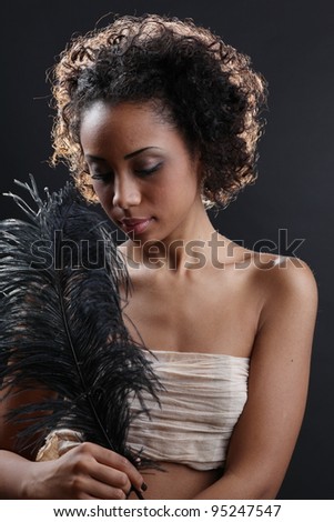 Beautiful black woman posing in a studio playing with a black feather.