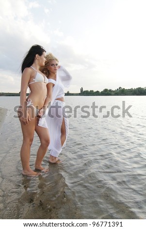 Two beautiful girls posing in the warm water at sunset