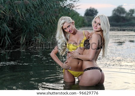 Two beautiful girls posing in the warm water at sunset