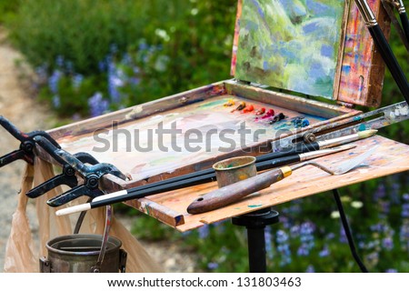 Box easel with canvas, oil paint, palette, and tools of an artist.  Landscape of mountain wildflowers on canvas.
