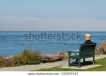 Older Man Sitting on a Bench Looking Out to Sea. Copy space.