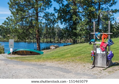 Water Safety. A rack holding life jackets stands lakeside near a canoe. Copy space.